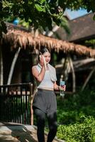 Woman in athletic wear with water bottle, enjoying a sunny day in a green park setting. photo