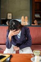 Woman in a cafe looking stressed, sitting with hand on forehead, reflecting in a cozy setting. photo