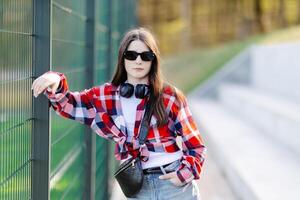 Teenager girl posing near metal fence wearing sunglasses and headphones photo