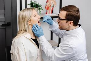 Doctor using inspection spatula to examine patient throat. ENT doctor doing throat exam of a woman. photo