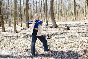 Young woman stretching in forest during nordic walking training photo