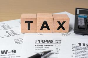 Filing taxes concept. Tax word on wooden cubes with calculator and pen placed on US 1040 income tax form for financial preparation photo