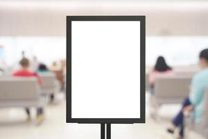 Blank vertical signage board mockup in hospital waiting area with blurred patients sitting in background scene photo