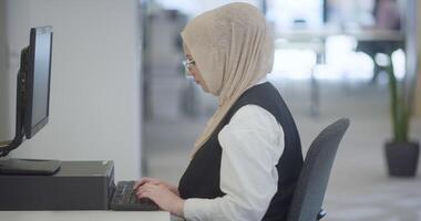 In a modern office, a Muslim entrepreneur wearing a hijab sits confidently and diligently works on her computer, embodying determination, creativity, and empowerment in the business world video