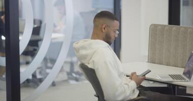 African American businessman wearing headphones while using a smartphone, fully engaged in his work at a modern office, showcasing focus, productivity, and contemporary professionalism video