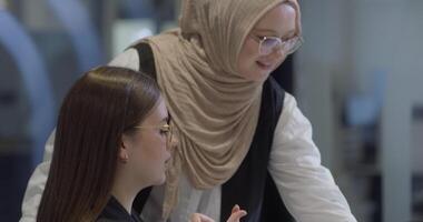 A diverse group of businesswomen, one of whom wears a hijab, collaborates while focusing on a laptop, engaging in discussions and problem-solving, showcasing professionalism, teamwork, and effective video