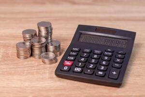 Finance, business, budget or investment concept. Stack of coins and calculator on wooden table. photo