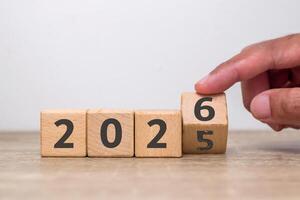 Hand flipping of 2025 to 2026 on wooden blocks with the number five already faded. Turn of the new year. New year's resolution. photo