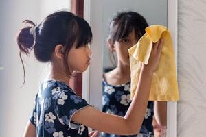 A young Asian girl cleaning the mirror in the wardrobe with a chamois cloth photo