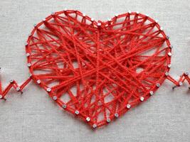 Creative heart design crafted from red yarn, adorned with shiny beads, showcasing intricate patterns and detailing that highlight artistic expression and craftsmanship in textile art photo