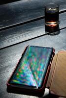 Spectrum blur reflection in glossy surface of smartphone on black table with alcohol drink shot photo