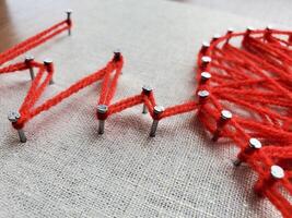 Creative string art project featuring vibrant red yarn and nails on fabric, depicting geometric patterns in numerous shapes and lines, showcasing artistic expression and craftsmanship skills photo