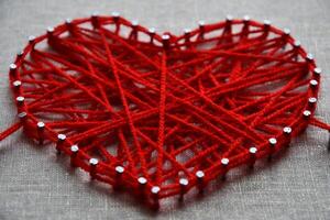 Red heart string art made with tangled yarn on metal nails on canvas background photo