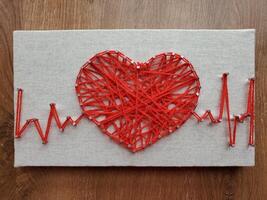Heart crafted with vibrant red string art displaying heartbeat rhythm on textured canvas surface showcasing intricate design and creative expression using simple materials and colors photo
