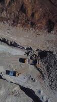 Quarry mining, work of the excavator and dump trucks, aerial view. Vertical video