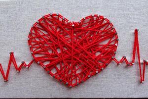 Red heart and heartbeat lines string art made with tangled red yarn on metal nails at canvas texture photo