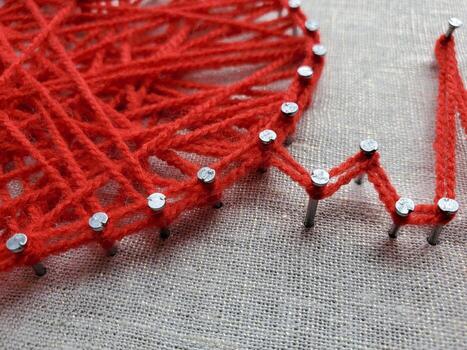 creativo hilo Arte proyecto exhibiendo intrincado modelo creación utilizando brillante rojo hilo herida alrededor metal patas, conjunto en contra un texturizado tela antecedentes durante tarde elaboración sesión foto