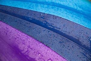Wet waterproof textile surface of blue gradient colored umbrella under drizzle rain. Water drops dripping at blue purple umbrella fabric texture. Rainy weather abstract background photo