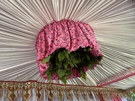 Pink floral canopy decoration with lush green foliage hangs from a pleated white ceiling. photo
