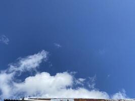Bright blue sky with fluffy white clouds above a weathered corrugated metal roof line. photo