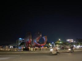 Illuminated abstract sculpture graces a roundabout at night with blurred motion and city lights. photo