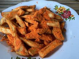 Golden fried potato wedges dusted with savory orange seasoning on a patterned plate. photo