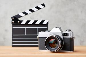 Vintage camera positioned on wooden table beside a classic film clapperboard, showcasing the essence of photography and filmmaking in a creative workspace environment photo