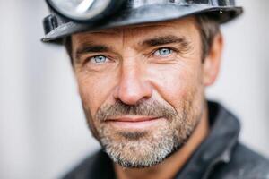 Caucasian man with blue eyes wearing a mining helmet and black work attire, poses confidently, showcasing the strength and determination of a skilled miner in an industrial environment photo
