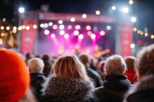 Crowd of concertgoers enjoying live music performance at night, illuminated stage with colorful lights, creating a vibrant atmosphere of excitement and energy photo