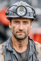 Male miner with blue eyes, wearing a hard hat and work clothes, stands confidently in a mining environment, showcasing dedication and resilience in the mining industry photo
