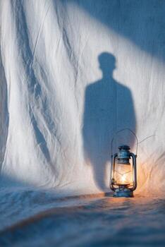 Vintage lantern casting a soft glow on textured fabric backdrop, with a shadow silhouette creating an intriguing atmosphere of warmth and nostalgia photo