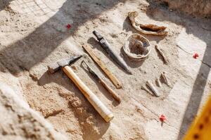 Archaeological excavation site featuring various ancient tools and artifacts arranged on sandy ground, showcasing historical significance and the process of discovery in archaeology photo