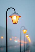 Street lamps illuminated at dusk create a warm glow in a foggy urban environment, enhancing the atmosphere and inviting a sense of tranquility and reflection in the scene photo