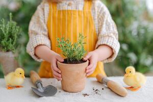 Child in yellow apron holds a terracotta pot with fresh herbs, surrounded by gardening tools and adorable ducklings, creating a joyful spring gardening atmosphere photo