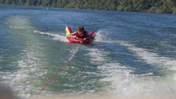 Teenager wearing a life jacket tubing on open water, holding onto a towable inflatable tube with a rope connection to a boat video
