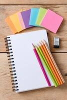 Colorful stationery items including a blank notebook, vibrant colored pencils, and sticky notes arranged on a wooden surface, ideal for creative projects and organization photo