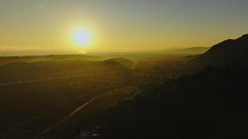 Aerial footage - Sunlight illuminating a mountain valley reveals a village and highway below during the enchanting golden hour. Spain, Valencia, Denia video
