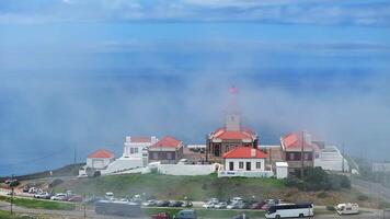 Clouds are moving around a lighthouse on a sunny day, while tourists and buses are parked nearby video