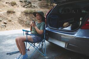 Woman Relaxing Outdoors with a Beverage Near an Open Car Trunk During a Hiking Adventure photo