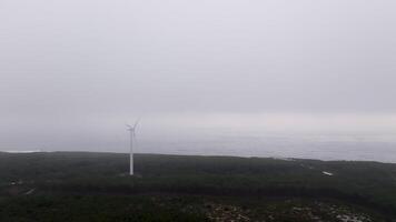 Wind turbine stands on a cliff overlooking the ocean, surrounded by fog on a tranquil day video