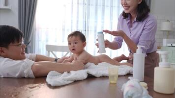 A tiny child happily on the towel waiting for parents apply powder and put on clothes after taking a bath video