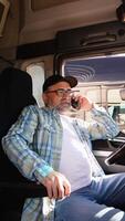 Senior trucker talking on the phone with a customer while sitting in his truck. Vertical video