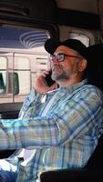 Senior trucker talking on the phone with a customer while sitting in his truck. Right hand drive car. Vertical video