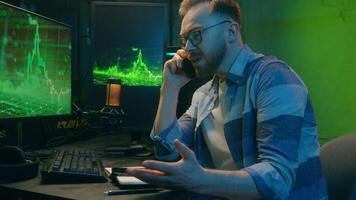 Stressed Caucasian man guy programmer freelancer crypto trader speak two mobile phones multitasking at home neon light negotiations tired male working at night computer pc business consult e-commerce video