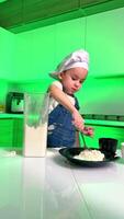 Young chef playing with flour. A child in chef attire mixes flour in a bright green kitchen space, showcasing creativity and culinary exploration. video
