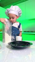 Young chef enjoys baking with flour. A toddler wearing a chef hat and apron plays with flour in a kitchen while filling a cup, creating a fun mess. video