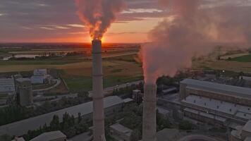 setting sun behind of smoke out of concrete factory pipe, drone view, such wow video