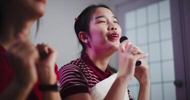 Handheld low angle view shot, Two women sitting on a sofa happily singing karaoke with smiles and enjoying a fun time together at home. Share good times video