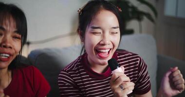 Two happy women sitting on a sofa happily singing karaoke with smiles and enjoying a fun time together at home. Share good times video
