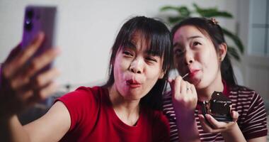 Handheld shot, Asian siblings sit on a sofa and use cell phone to talk to friends via call in a cozy living room. Share good times video